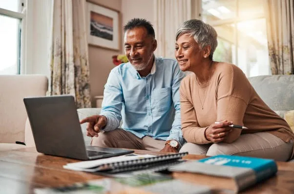 A couple smiling over their plan at the laptop